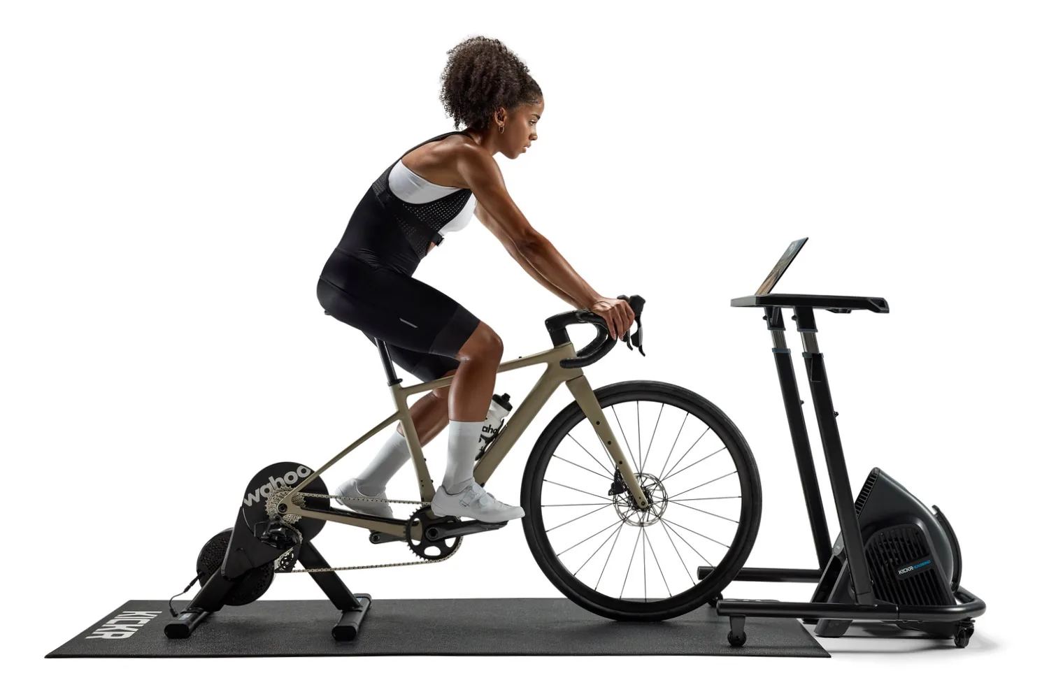 Indoor cycling setup with a Wahoo KICKR smart trainer plus accessories including heart rate monitor, KICKR desk, HEADWIND fan, pedals, and mat